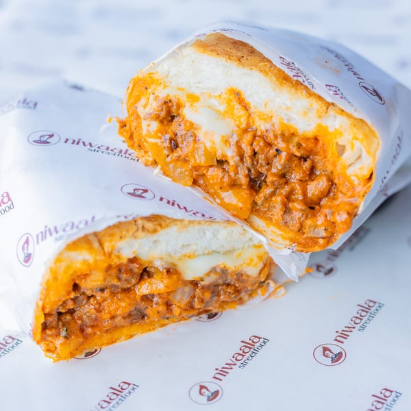 Halved sandwich with savory meat and cheese filling, wrapped in Niwaala Streetfood branded paper.
