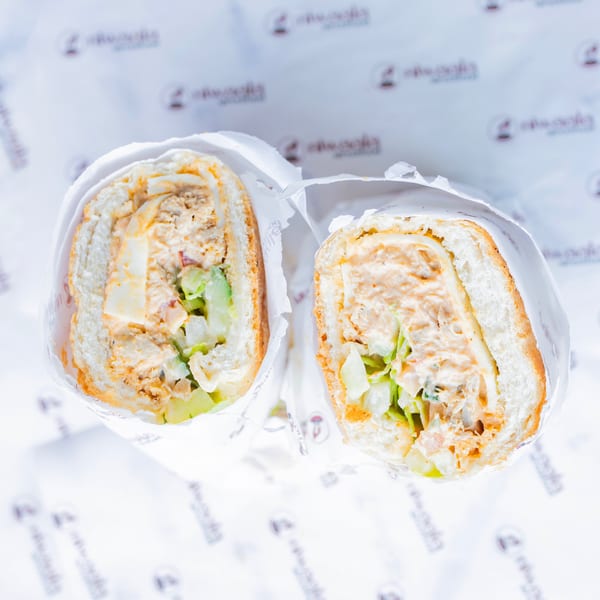 Two halves of a creamy salad sandwich with lettuce and egg, wrapped in branded white paper.