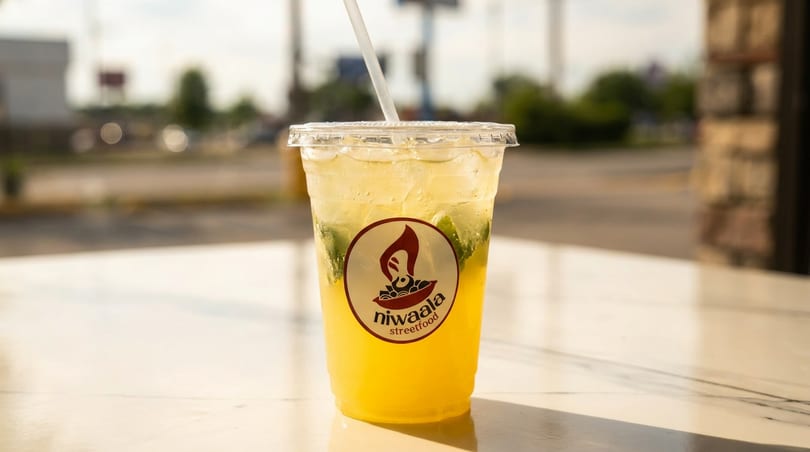 A refreshing yellow drink with mint and ice, branded with the Niwaala Streetfood logo, on a sunny patio.