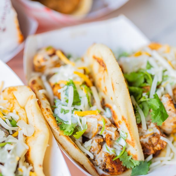 Grilled chicken tacos with cheese, cilantro, and white sauce in paper trays.
