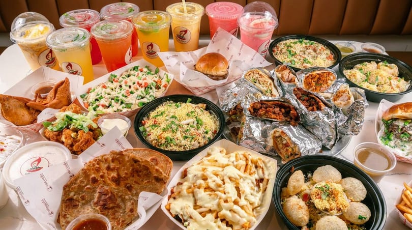 A table laden with various dishes including wraps, burgers, fries, salads, and colorful drinks.