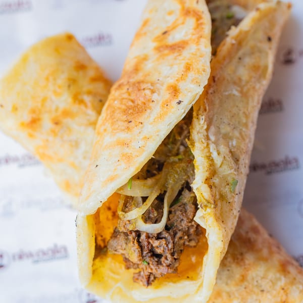 Two golden-brown flatbread wraps filled with seasoned meat and onions on branded paper.
